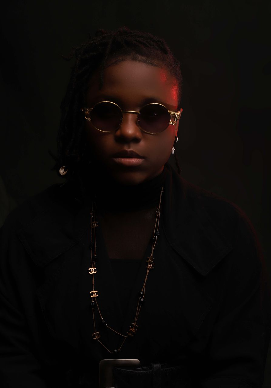 Adora looking strtaight at the camera wearing black clothes, glasses and fabulous jewelry
